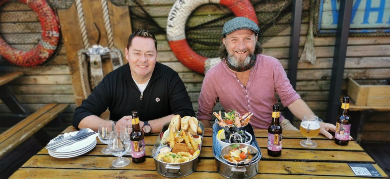 two people sitting at a table with food and drinks on front of them